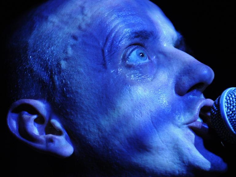 Sänger Kai-Uwe Kohlschmidt (Sandow) beim Konzert in Erfurt 2008. Ein von Bühnenlicht blau beleuchteter kahler Schädel mit weit aufgerissenem Auge singt in ein Mikrofon.