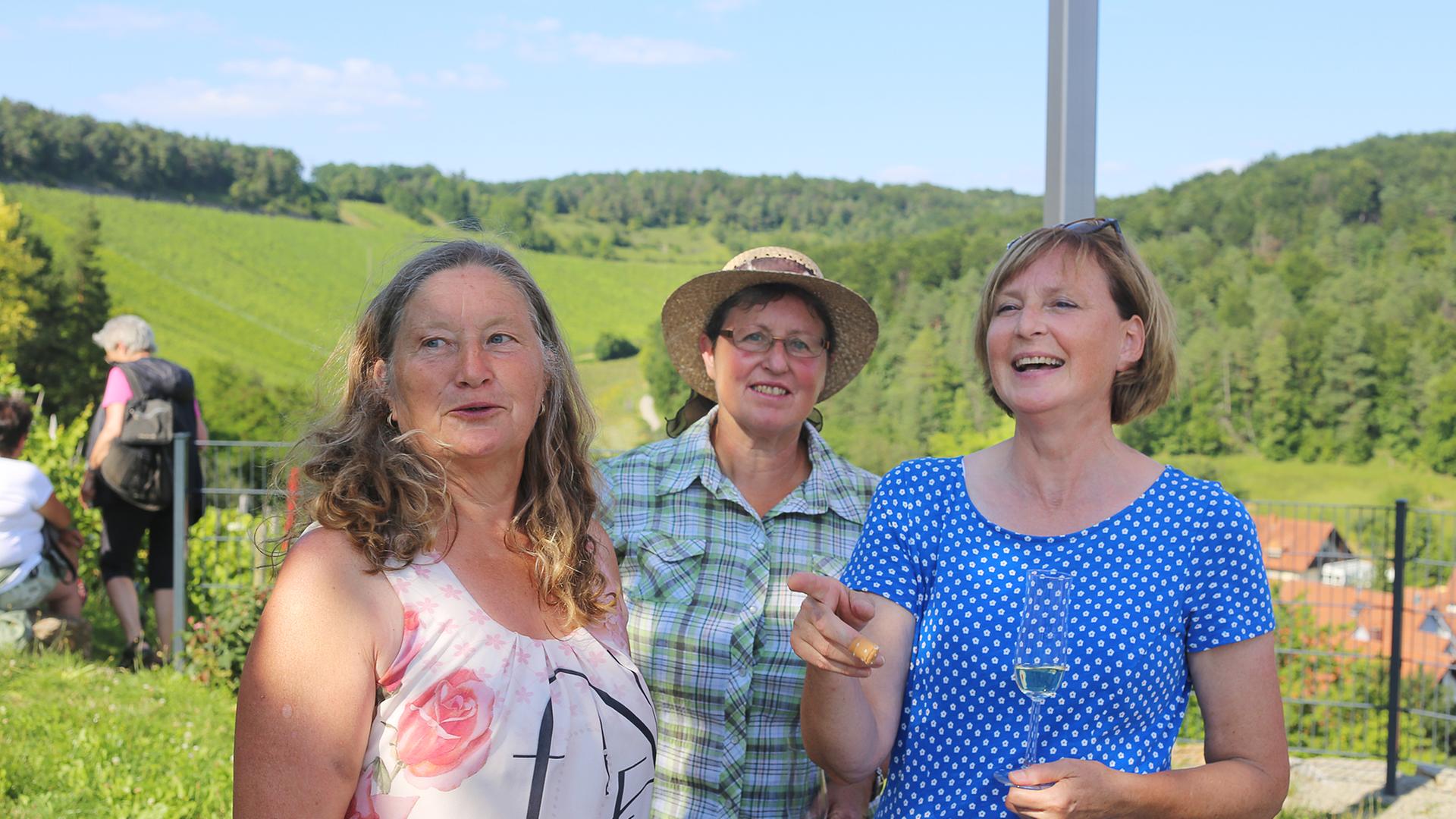 Drei Landfrauen stehen zusammen, im Hintergrund sind Felder und Wald zu erkennen. Drei Landfrauen stehen zusammen, im Hintergrund sind Felder und Wald zu erkennen.