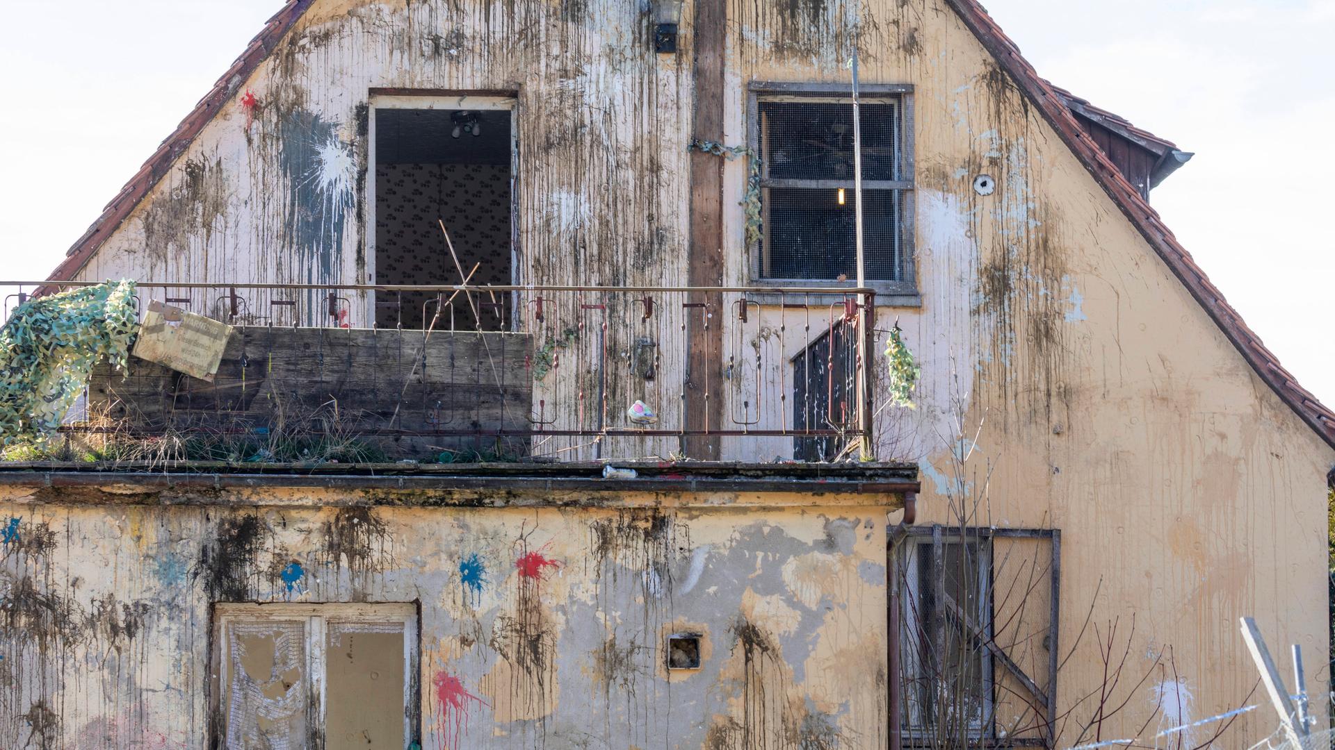 Frontalansicht der Fassade eines Hauses im desolaten Zustan, das mit zahlreichen Farbbeutel beworfen wurde.