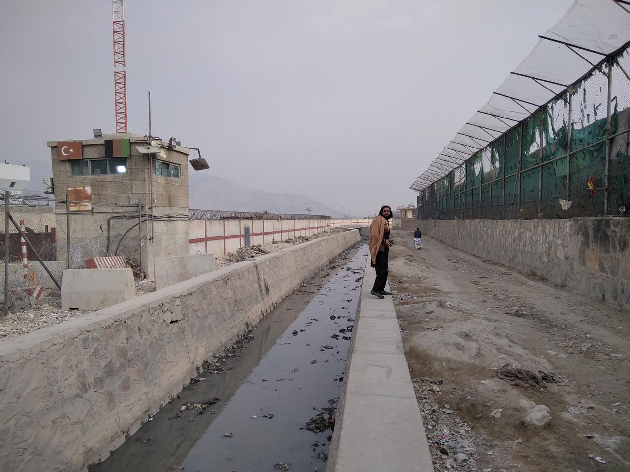 Ein Taliban-Kommandeur zeigt die Stelle am Flughafens, wo im August 2021 der Sprengstoffanschlag stattfand. Die US-Soldaten vor der Mauer und viele Zivilisten wurden in den Entwässerungskanal geschleudert, wo sich noch immer Überreste finden. Ein Taliban-Kommandeur zeigt die Stelle am Flughafens, wo im August 2021 der Sprengstoffanschlag stattfand. Die US-Soldaten vor der Mauer und viele Zivilisten wurden in den Entwässerungskanal geschleudert, wo sich noch immer Überreste finden.