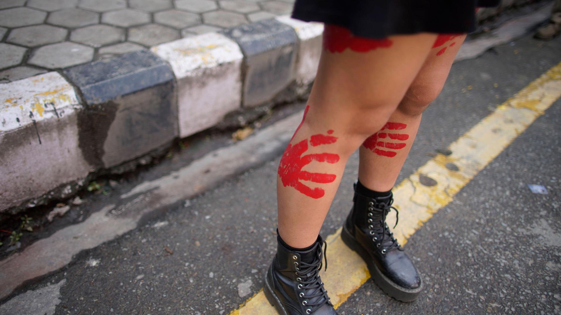 Eine junge Frau demonstriert in Nepal gegen sexualisierte Gewalt mit roten Handabdrücken auf den nackten Beinen. Eine junge Frau demonstriert in Nepal gegen sexualisierte Gewalt mit roten Handabdrücken auf den nackten Beinen.