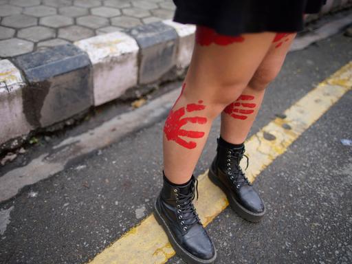 Eine junge Frau demonstriert in Nepal gegen sexualisierte Gewalt mit roten Handabdrücken auf den nackten Beinen.