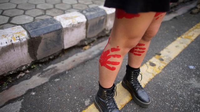 Eine junge Frau demonstriert in Nepal gegen sexualisierte Gewalt mit roten Handabdrücken auf den nackten Beinen.