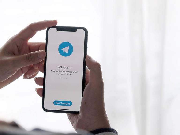 Eine hand hält ein Smartphone mit der geöffneten Telegram-App