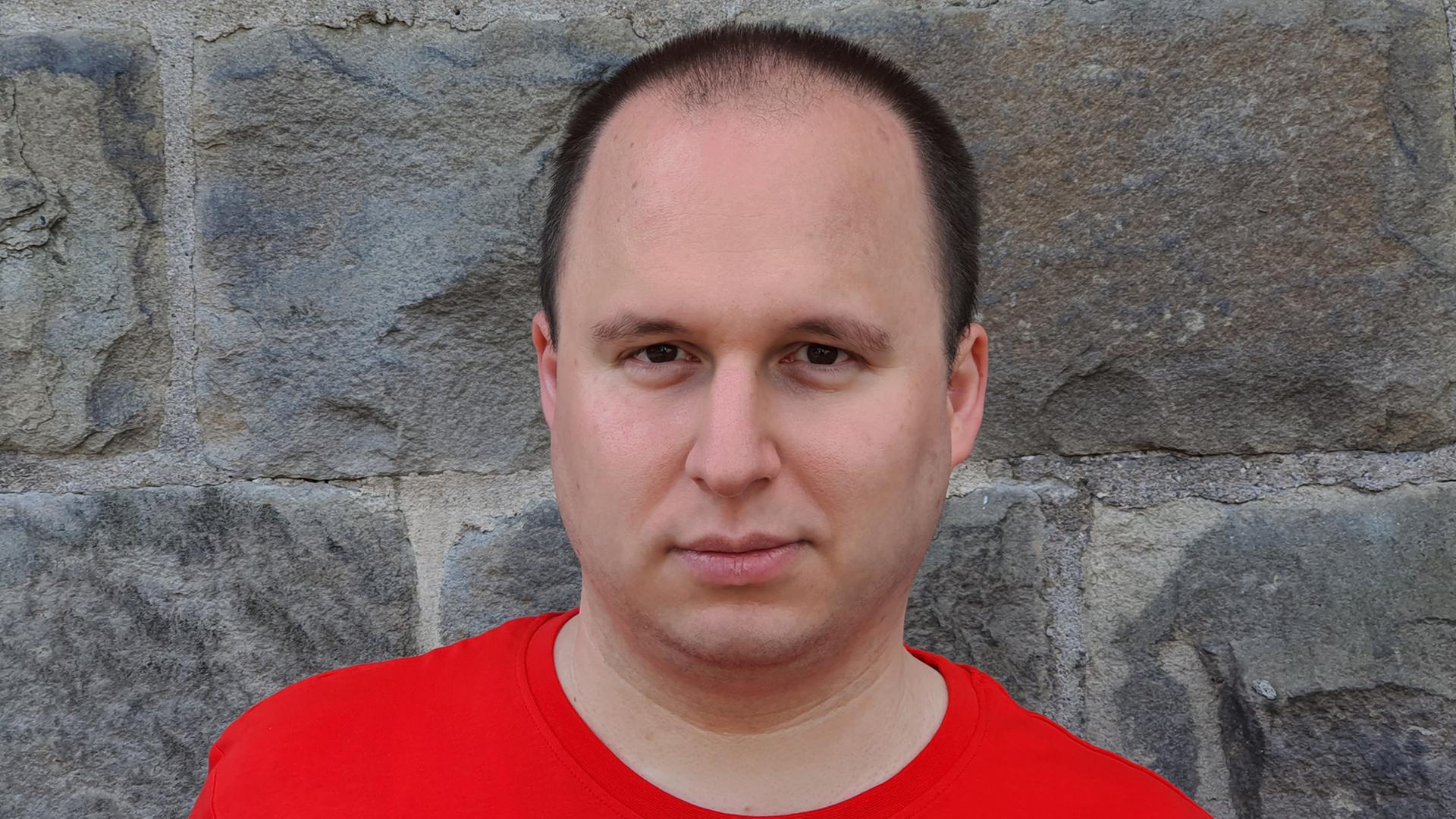 Martin Tchiba steht in rotem T-Shirt vor einer Wand Martin Tchiba steht in rotem T-Shirt vor einer Wand