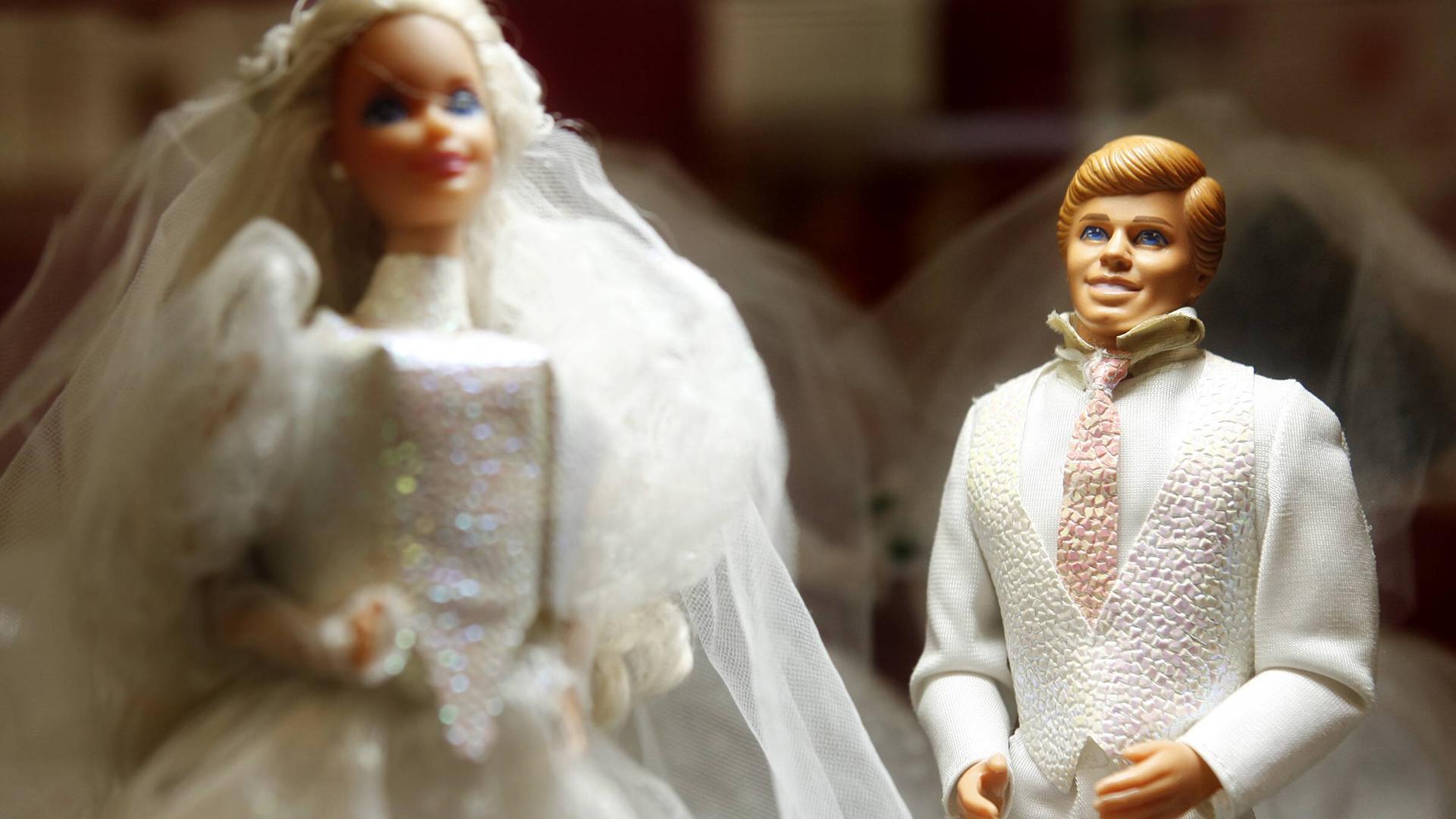 Das Bild zeigt eine Barbie- und eine Ken-Puppe in weißer Hochzeitskleidung.