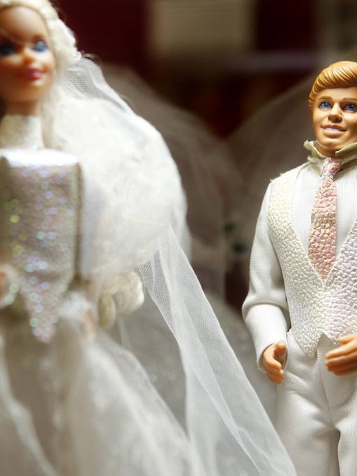 Das Bild zeigt eine Barbie- und eine Ken-Puppe in weißer Hochzeitskleidung.