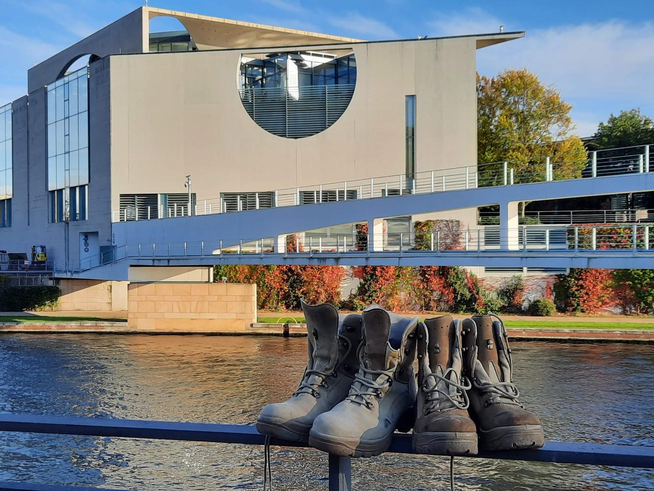 Auf einem Geländer stehen zwei Paar robuste Stiefel, im Hintergrund ist das Bundeskanzleramt zu sehen.