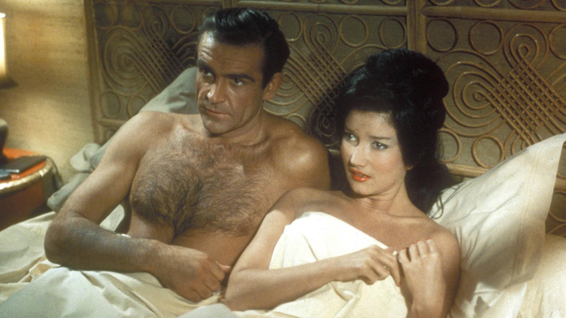 Szene aus dem James-Bond-Film "Dr. No": Der Schauspieler Sean Connery als Agent 007 liegt neben einer Frau in einem Bett. Szene aus dem James-Bond-Film "Dr. No": Der Schauspieler Sean Connery als Agent 007 liegt neben einer Frau in einem Bett.