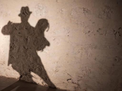 Ein tanzendes Tangopaar wirft seine Schatten auf eine grobe Wand.