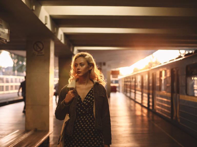 Eine junge Frau steht erschöpft an einem Bahngleis.