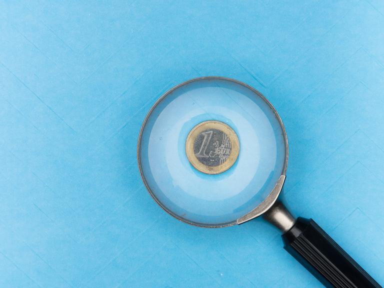 Ein-Euro-Münze unter einer Lupe auf blauem Grund.