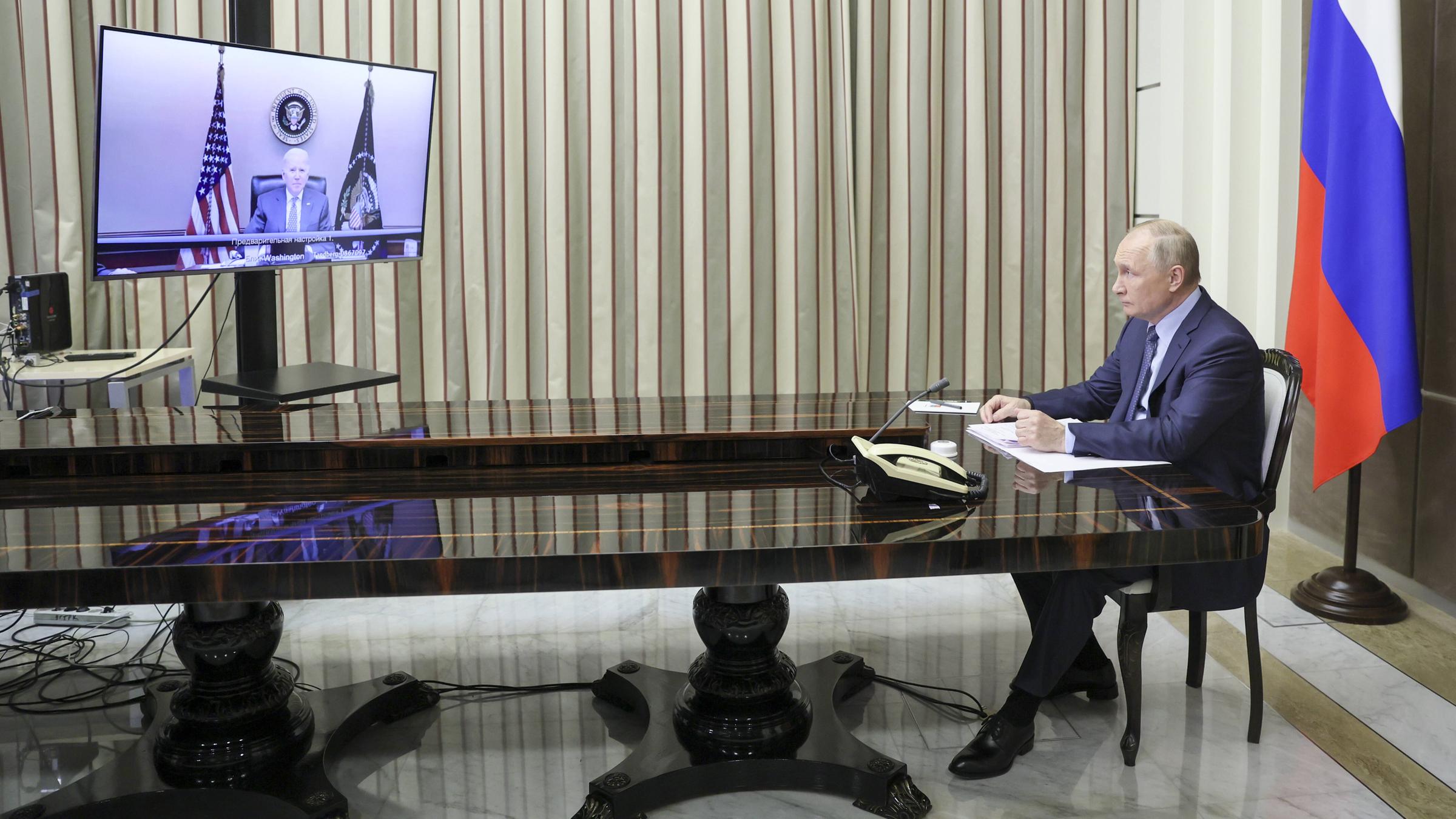 Der russische Präsident Vladimir Putin sitzt an einem langen, mächtigen Tisch und schaut auf einen Bildschirm, auf dem der amerikanische Präsident Joe Biden zu sehen ist.<br/>