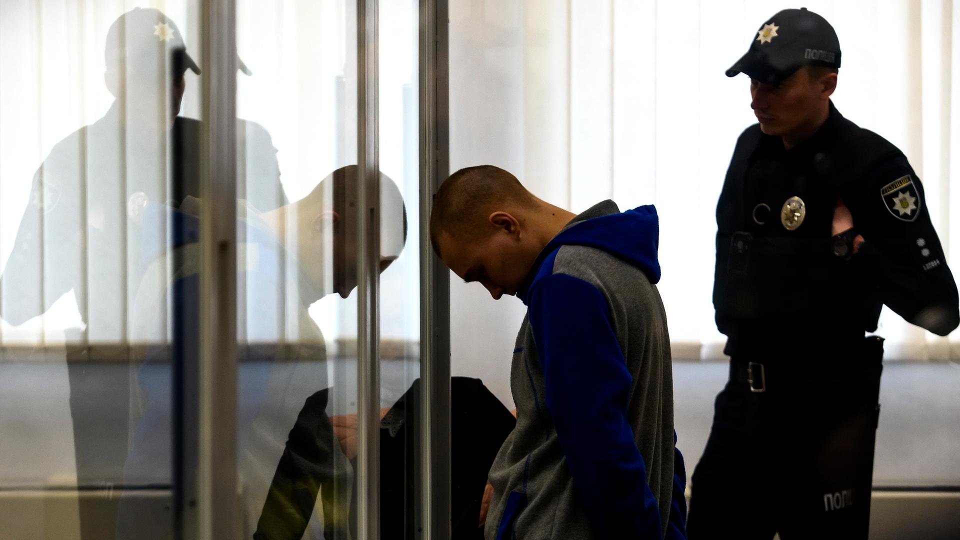 Der 21-jährige Russische Soldat, der verurteilt wurde, steht während des Prozess' mit gesenktem Kopf in einem Glaskasten. Der 21-jährige Russische Soldat, der verurteilt wurde, steht während des Prozess' mit gesenktem Kopf in einem Glaskasten.