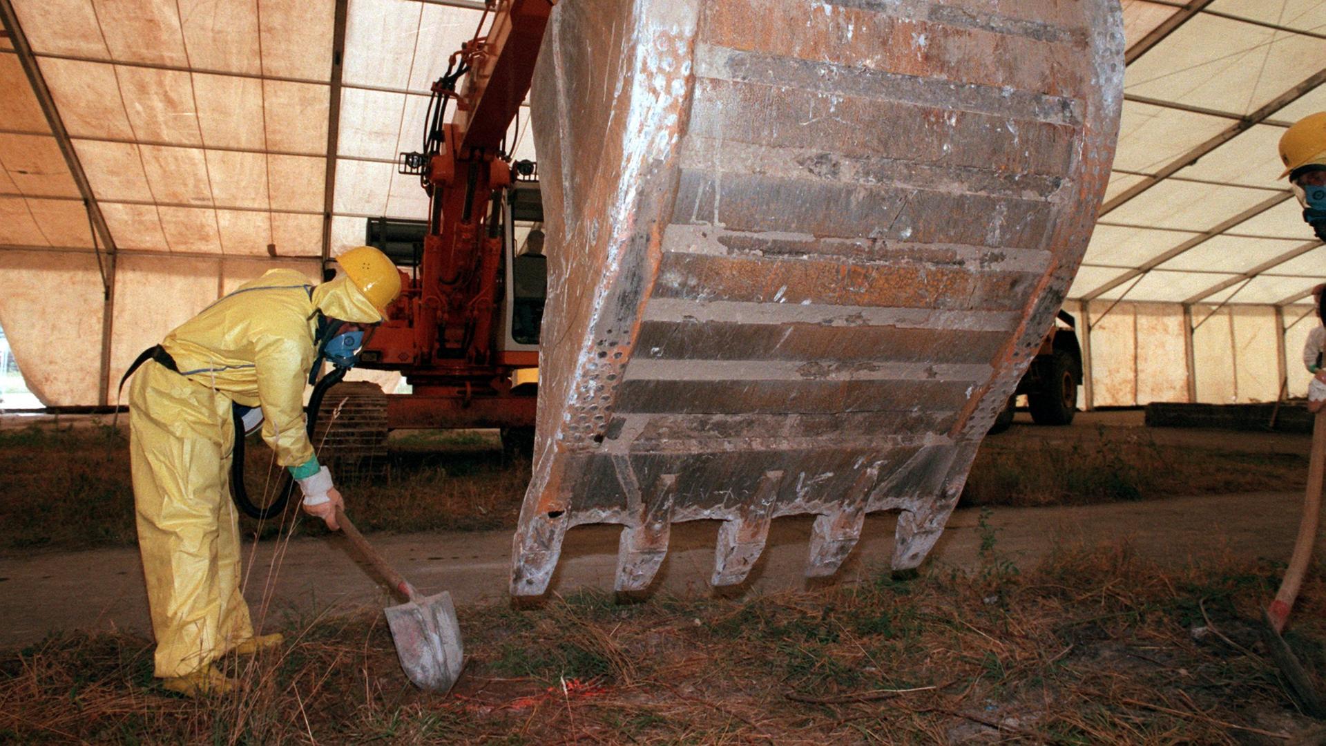 Ein Bagger und ein Arbeiter in einem Schutzanzug beseitigen etwas aus Erde.