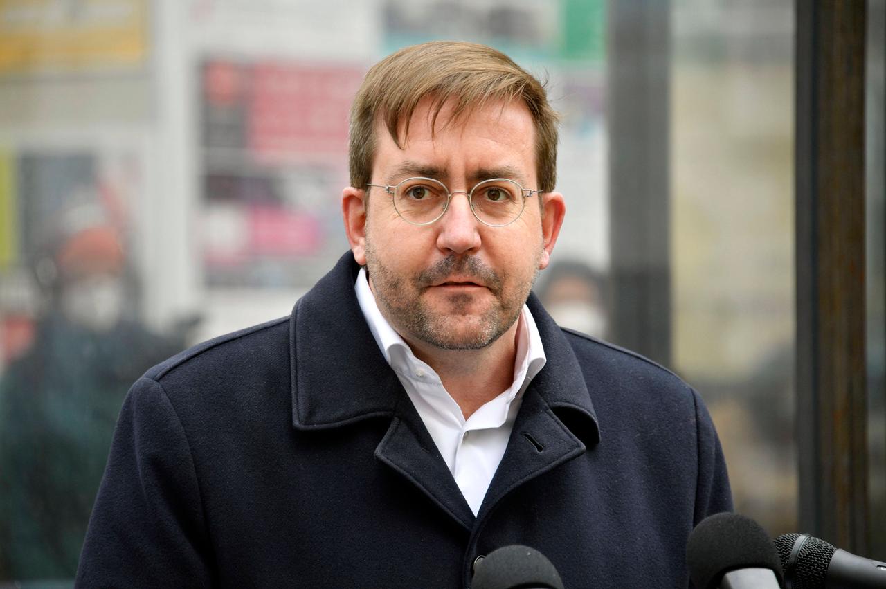 Christian Mihr, mit Brille, in einem schwarzen Mantel, steht im Freien vor drei Mikrofonen. Christian Mihr, mit Brille, in einem schwarzen Mantel, steht im Freien vor drei Mikrofonen.