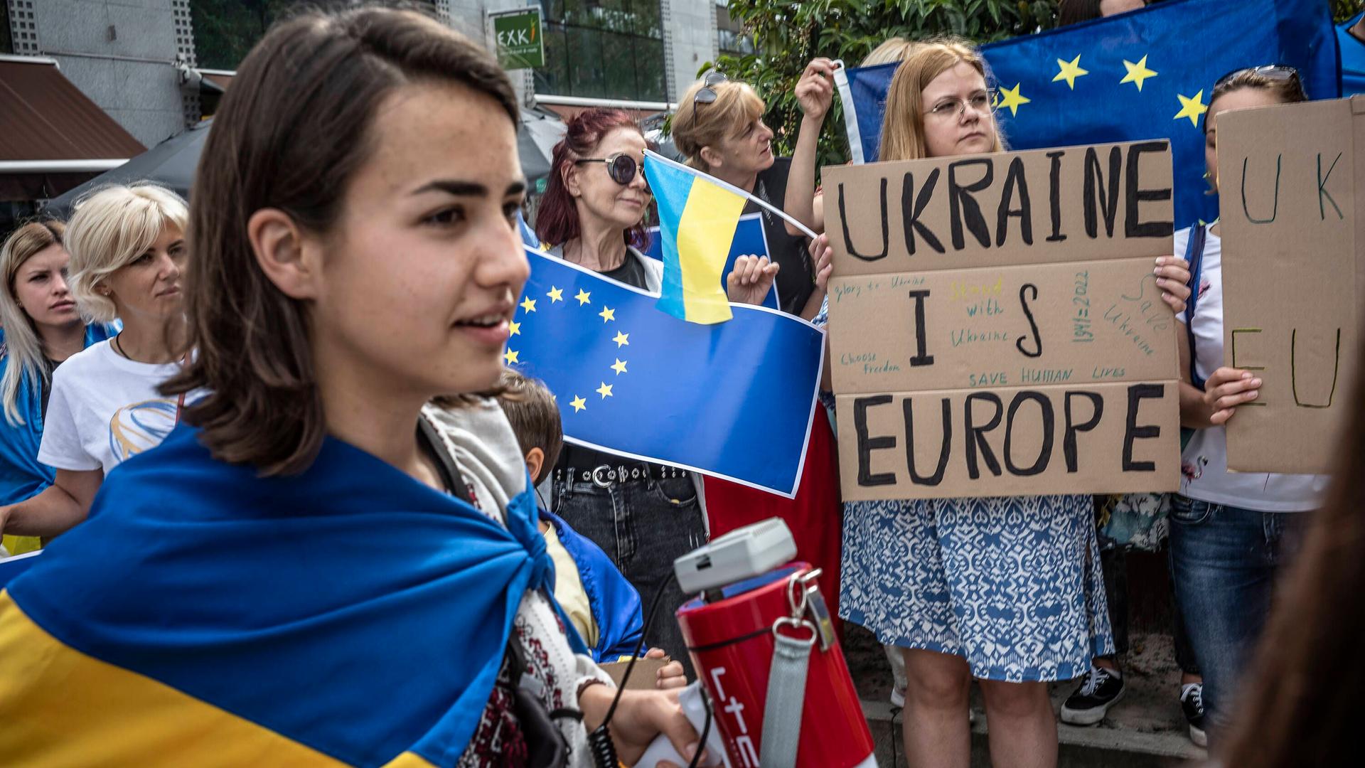 Teilnehmerinnen einer Protestaktion in Brüssel halten ukrainische Flaggen hoch und haben Plakate in der Hand Teilnehmerinnen einer Protestaktion in Brüssel halten ukrainische Flaggen hoch und haben Plakate in der Hand
