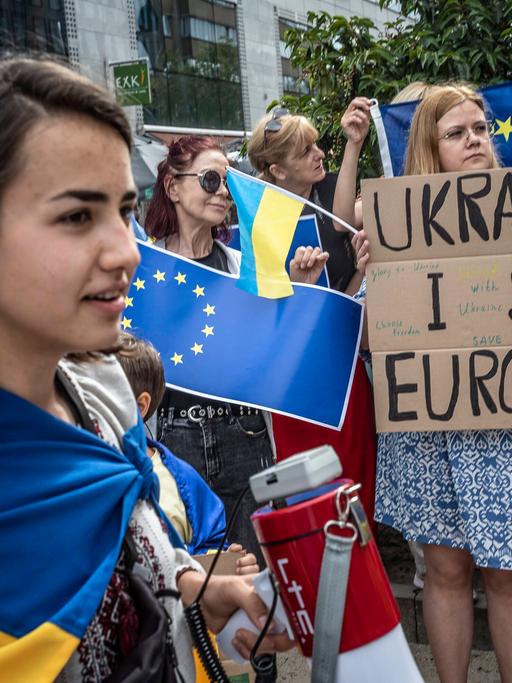 Teilnehmerinnen einer Protestaktion in Brüssel halten ukrainische Flaggen hoch und haben Plakate in der Hand