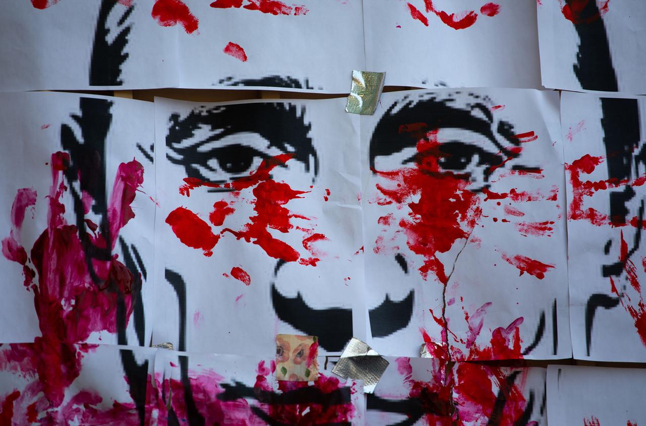 Rote Farbkleckse und Handabdrücke auf einer Zeichnung des Gesichts von Wladimir Putin.