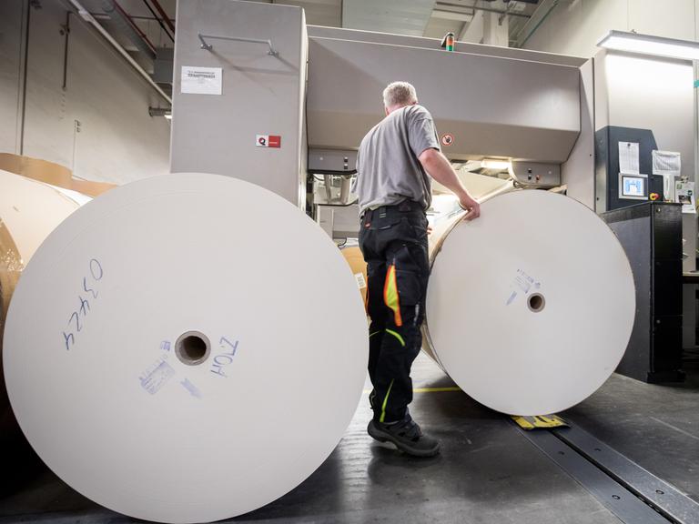 Ein Drucker wechselt in einer Druckerei Papierrollen für den Buchdruck in einer Druckmaschine.