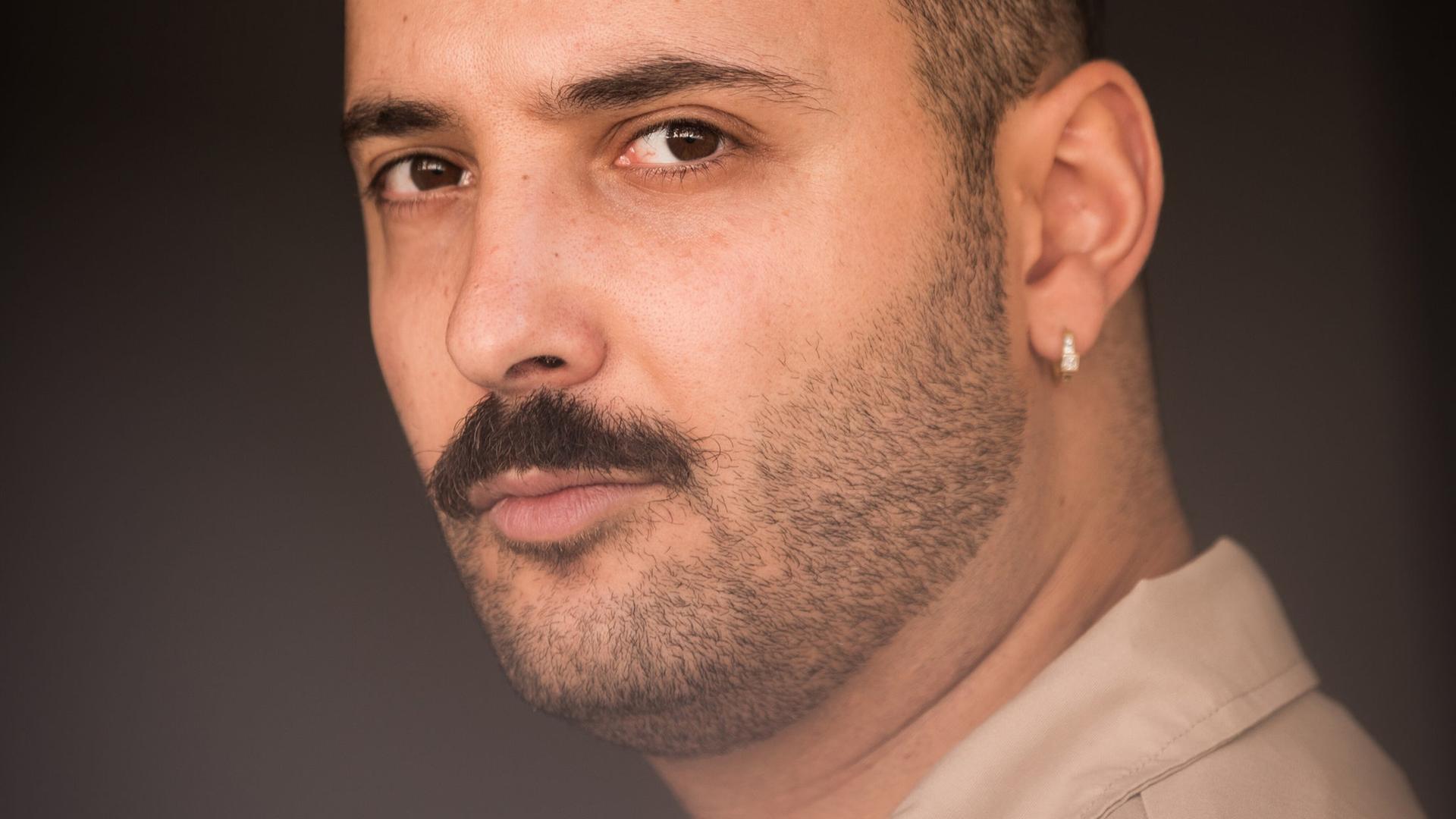 Fikri Anıl Altıntaş, ein junger Mann mit Schnurrbart und einem dezenten Ohrring im linken Ohr, schaut im Halbprofil entspannt in die Kamera. Fikri Anıl Altıntaş, ein junger Mann mit Schnurrbart und einem dezenten Ohrring im linken Ohr, schaut im Halbprofil entspannt in die Kamera.