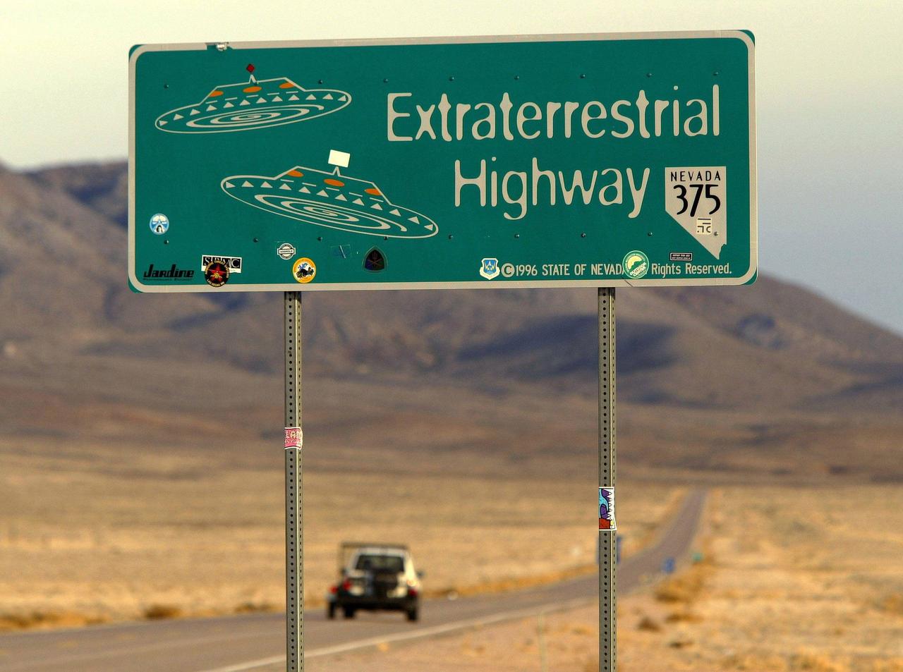 Straßenschild mit der Aufschrift "Extraterrestrial Highway" und Zeichnungen zweier UFOs in der Wüste von Nevada.