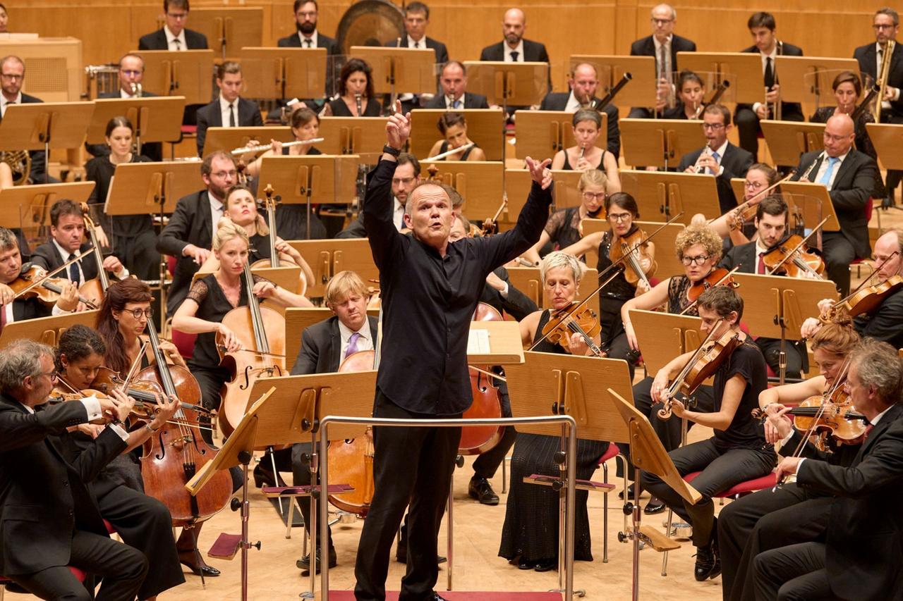 Ein Orchester. Im Vordergrund steht der Dirigent, er dreht sich zum Publikum um. Ein Orchester. Im Vordergrund steht der Dirigent, er dreht sich zum Publikum um.