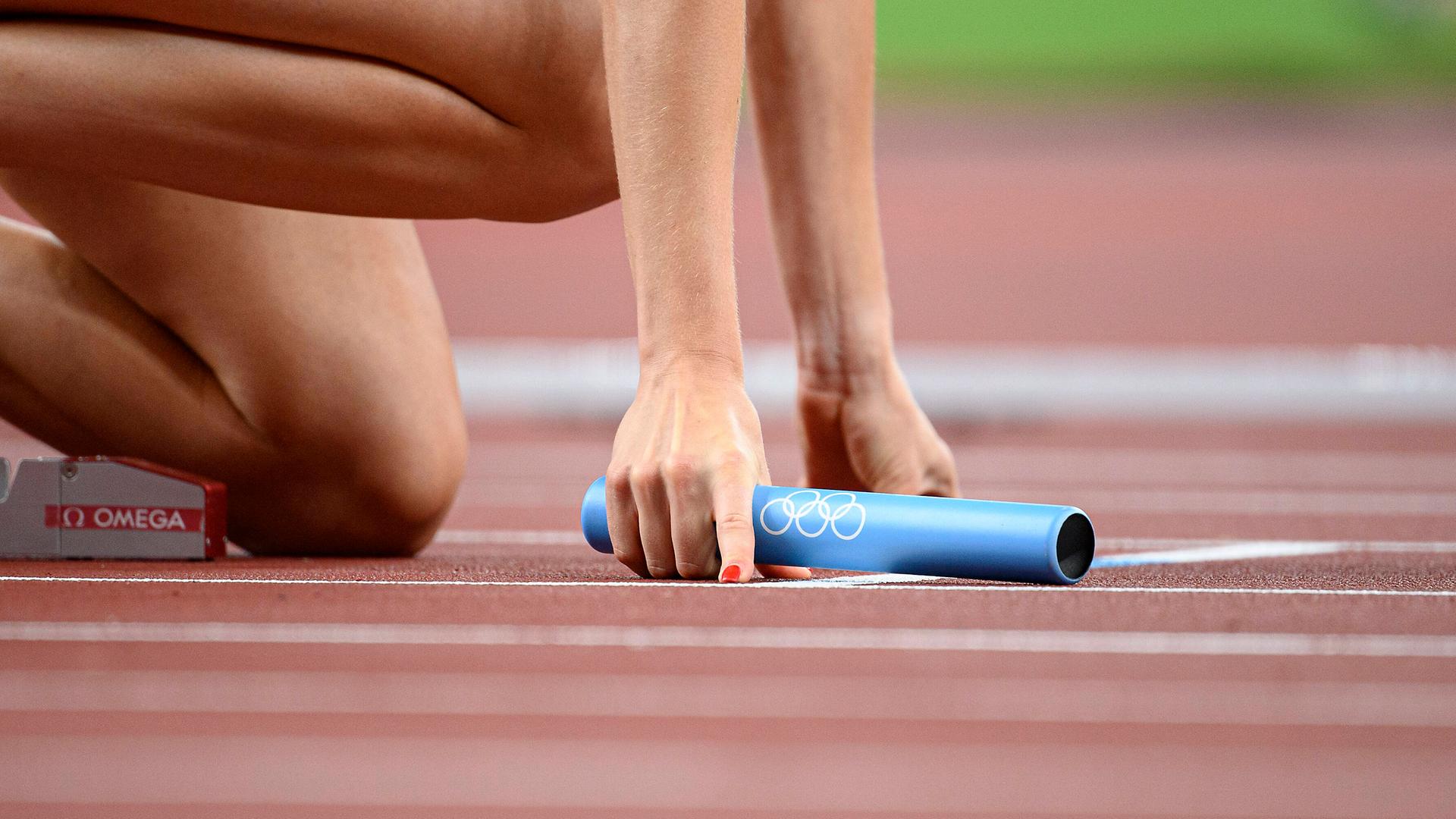 Eine Leichtathletin hält beim 4x400 Meter Staffellauf den Staffelstab beim Start in der rechten Hand.