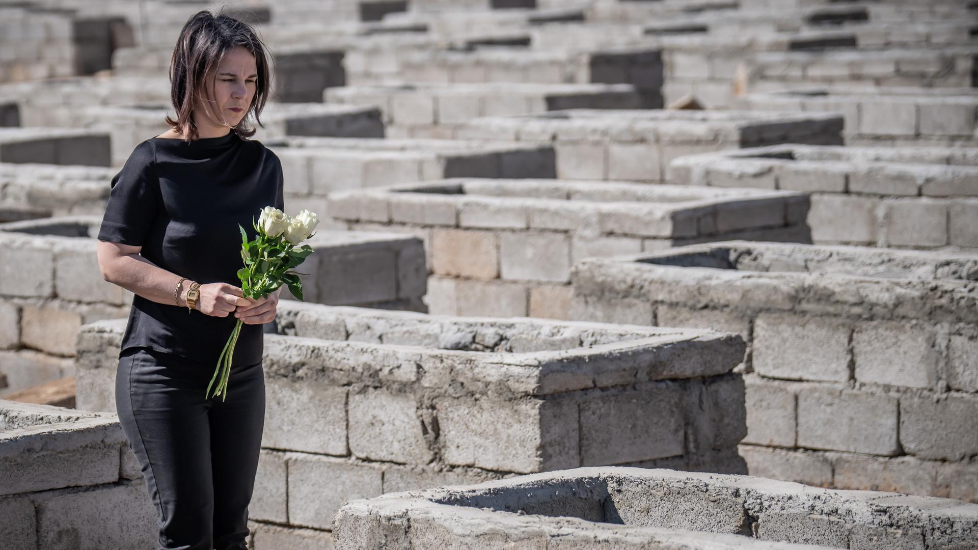 Bundesaußenministerin Annalena Baerbock legt weiße Blumen am Friedhof von Kocho nieder. 