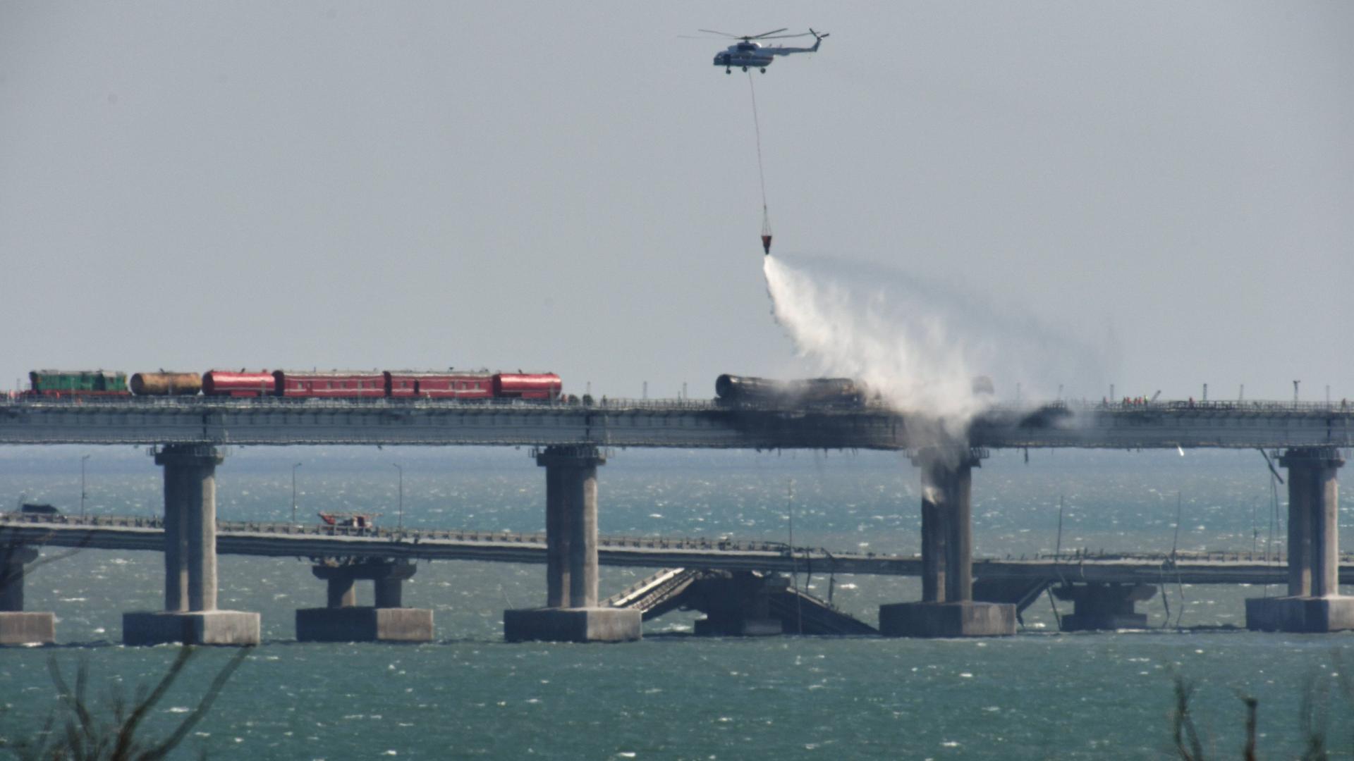 Das Foto zeigt die Kertschbrücke zwischen dem russischen Festland und der annektierten Krim. Ein Hubschauber wirft Wasser ab, um einen in Flammen stehenden Güterzug auf der Krim-Brücke zu löschen.