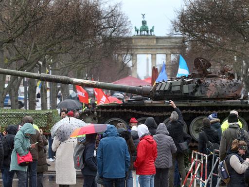 Passanten stehen vor einem in der Ukraine zerstörten russischen Panzer. Der Panzer T-72 steht auf einem Hänger vor der Botschaft Russlands Unter den Linden in Berlin. Diese Aktion soll ein Zeichen des Protests gegen den Krieg Russlands sein und soll die Solidarität mit der Ukraine ausdrücken. 