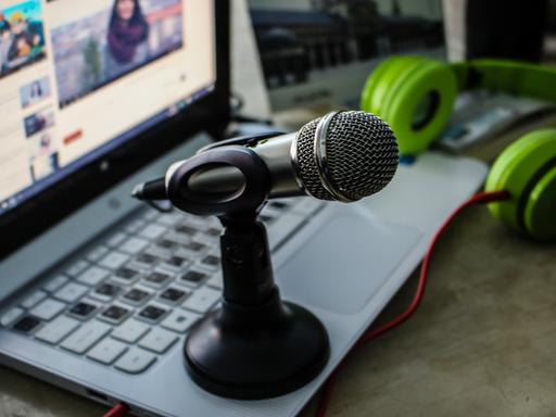 Ein Mikrofon steht auf einem Laptop, auf dem eine Video abläuft, in dem eine Reporterin zu sehen ist.
