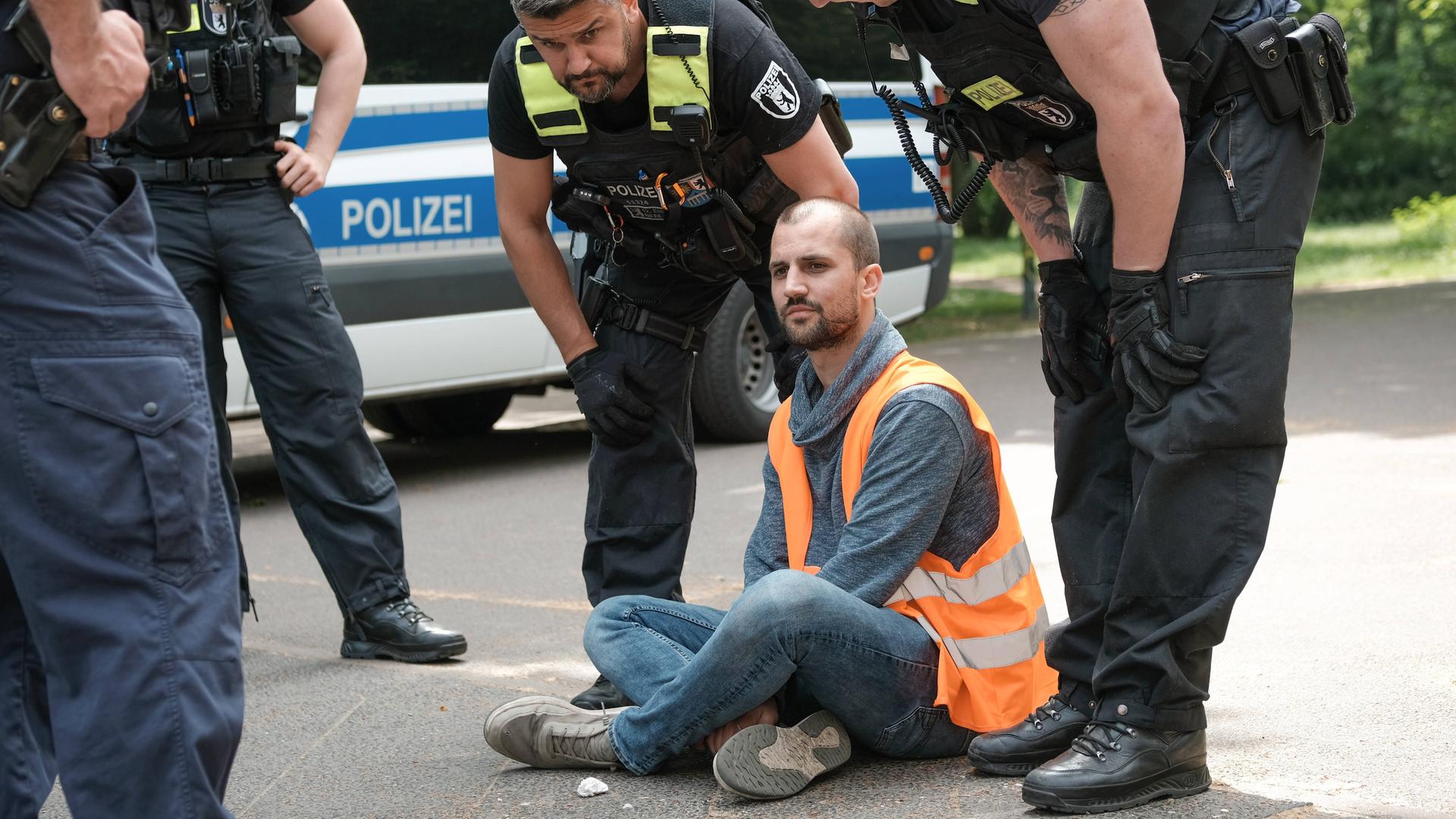 Polizisten sprechen mit einem Mann, der im Schneidersitz auf einer Straße in Berlin sitzt. Polizisten sprechen mit einem Mann, der im Schneidersitz auf einer Straße in Berlin sitzt.