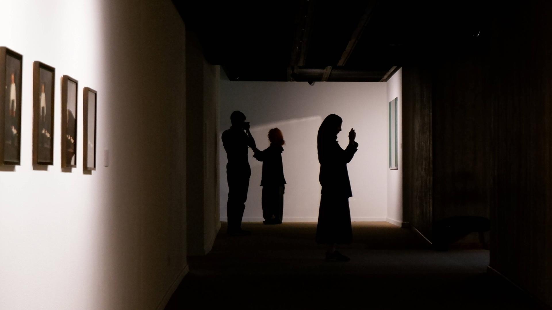 Zwei Frauen mit Kopftuch und ein Mann sind als Silhouetten in einer Kunstausstellung im Iran zu sehen. Zwei Frauen mit Kopftuch und ein Mann sind als Silhouetten in einer Kunstausstellung im Iran zu sehen.