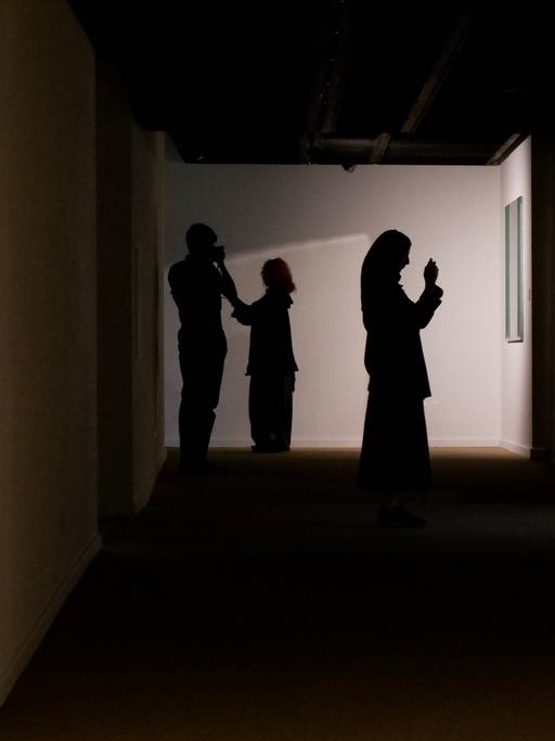 Zwei Frauen mit Kopftuch und ein Mann sind als Silhouetten in einer Kunstausstellung im Iran zu sehen.