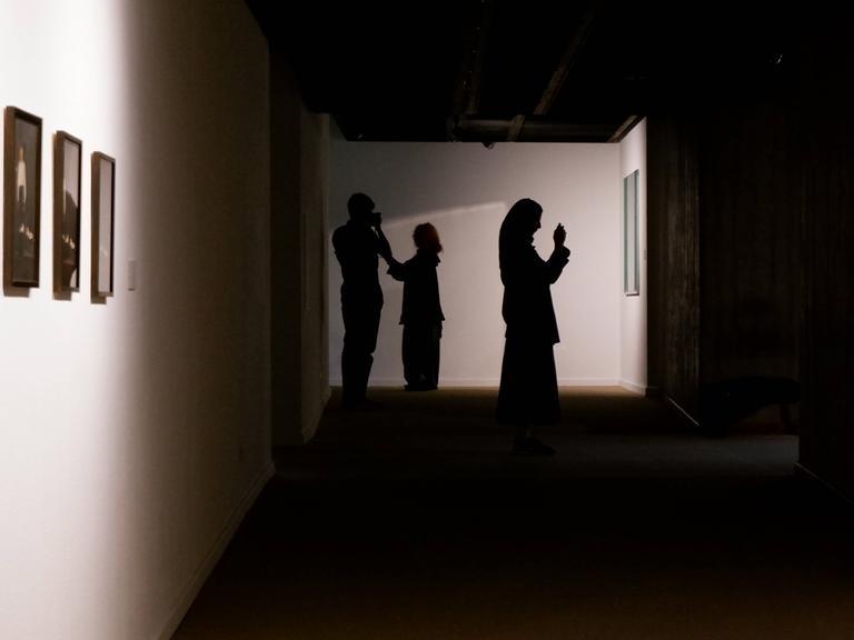 Zwei Frauen mit Kopftuch und ein Mann sind als Silhouetten in einer Kunstausstellung im Iran zu sehen.