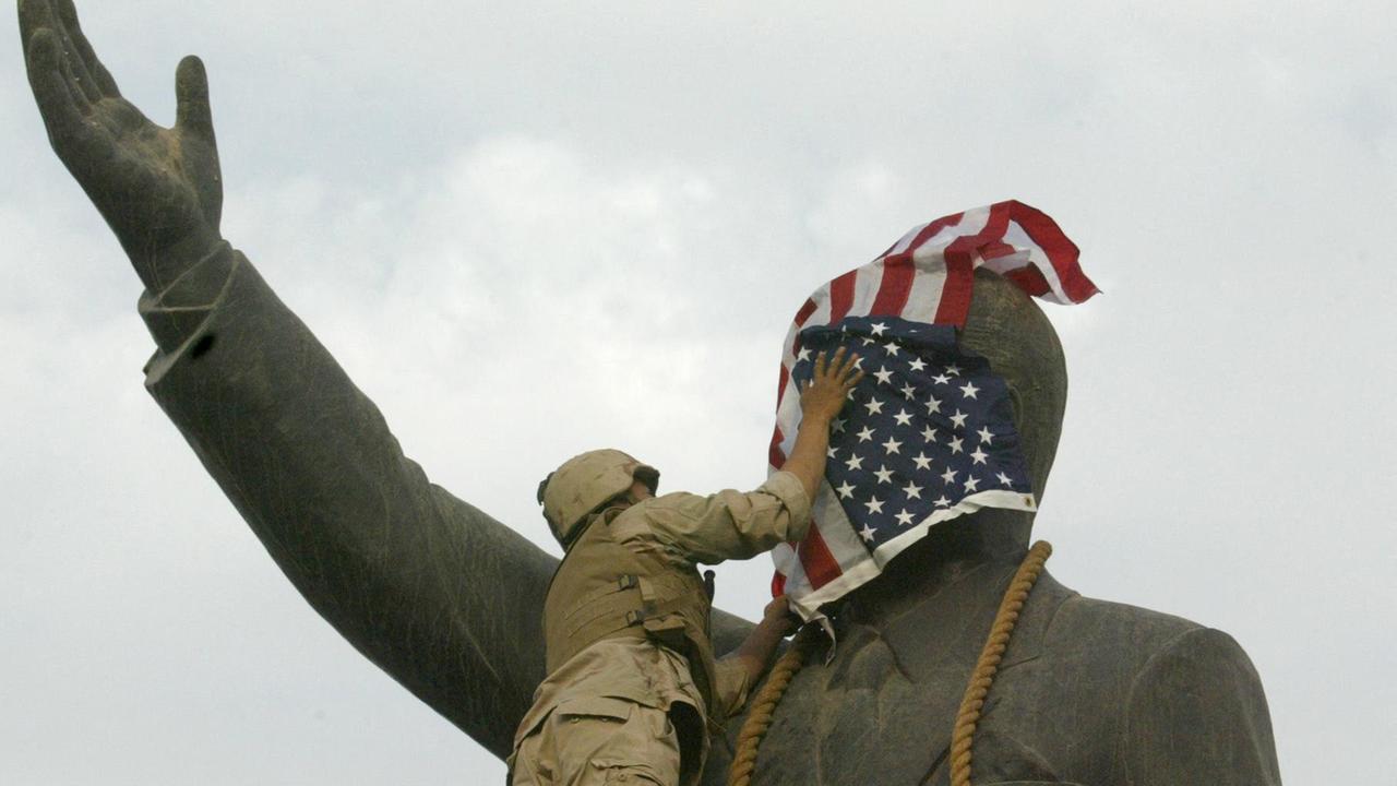 Das Foto zeigt einen US-Soldaten, der am 9. April 2003 das Gesicht der Statue des irakischen Präsidenten Saddam Hussein mit der US-Flagge auf dem al-Fardous-Platz in Bagdad bedeckt. Das Foto zeigt einen US-Soldaten, der am 9. April 2003 das Gesicht der Statue des irakischen Präsidenten Saddam Hussein mit der US-Flagge auf dem al-Fardous-Platz in Bagdad bedeckt.