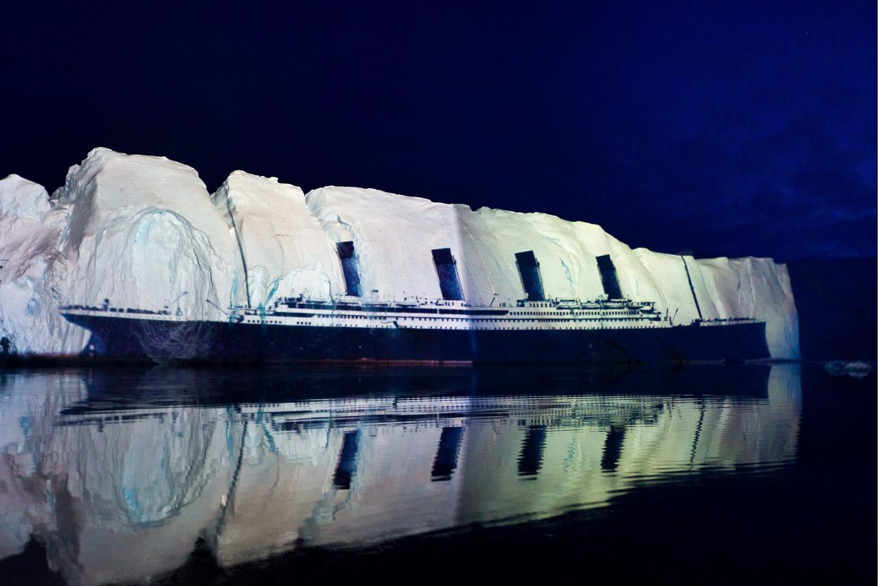 Auf dem nächtlichen Meer wird ein Bild des Übersee-Dampfers Titanic auf die Flanke eines Eisbergs projiziert. Auf dem nächtlichen Meer wird ein Bild des Übersee-Dampfers Titanic auf die Flanke eines Eisbergs projiziert.