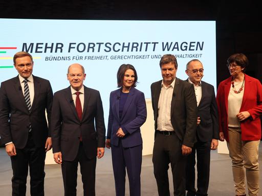 Von links nach rechts stehen Christian Lindner, Olaf Scholz, Annalena Baerbock, Robert Habeck, Norbert-Walter Borjans und Saskia Esken auf einer Bühne. Hinter ihnen die Aufschrift "Mehr Fortschritt wagen"