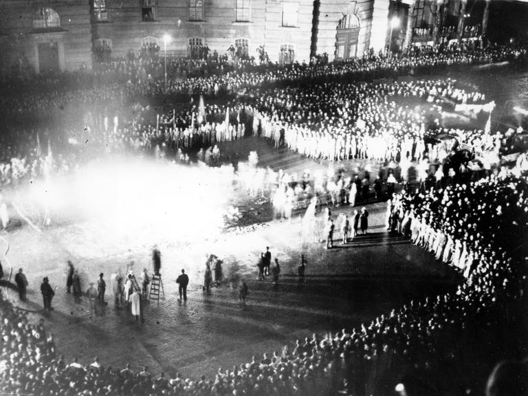 Historisches Schwarzweißfoto einer großen Menschenmenge, die um einen brennenden Scheiterhaufen herumsteht.