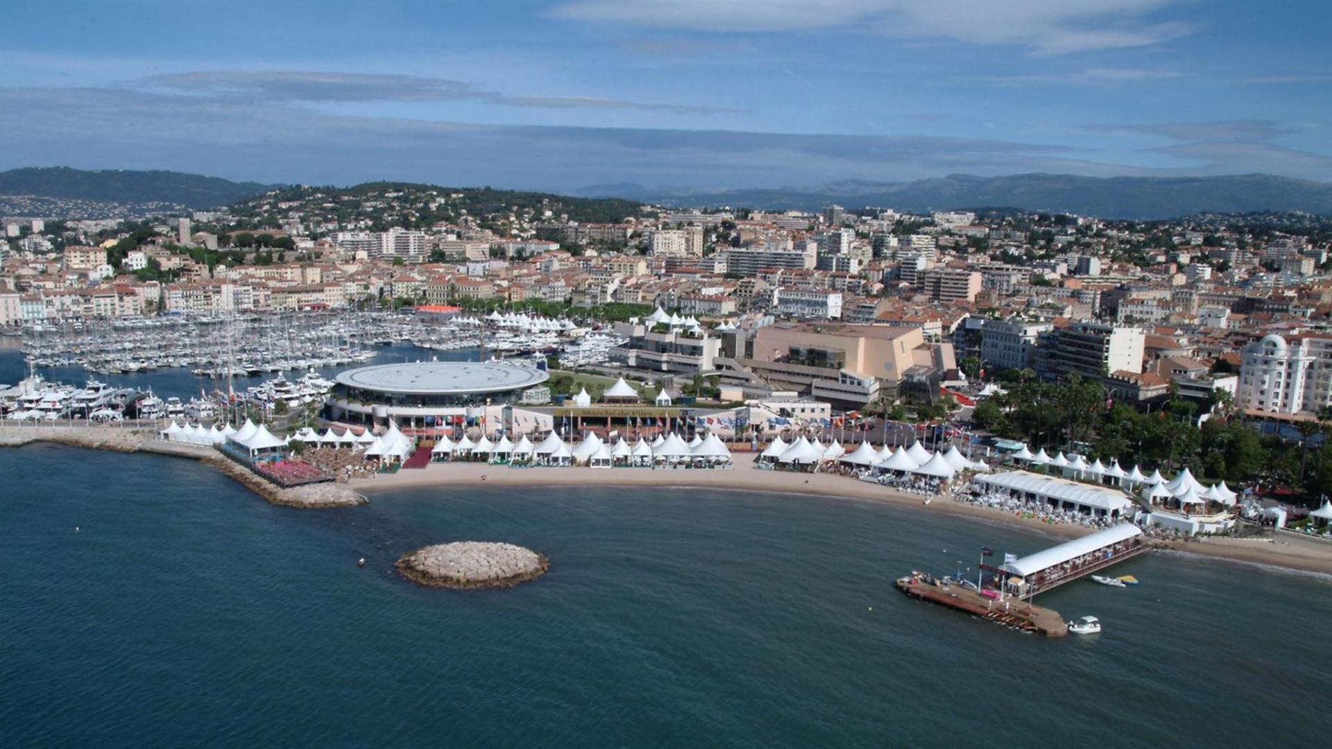 Panoramablick über das Küstenstädtchens Cannes mit vielen weißen Zelten am Strand und einem großen Festivalkino unweit davon.