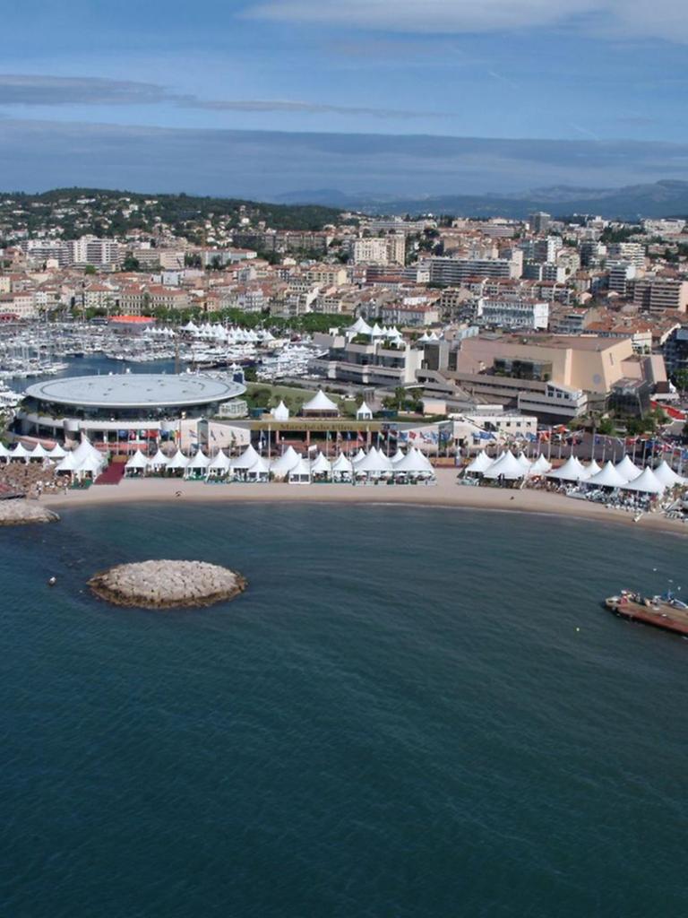 Panoramablick über das Küstenstädtchens Cannes mit vielen weißen Zelten am Strand und einem großen Festivalkino unweit davon.