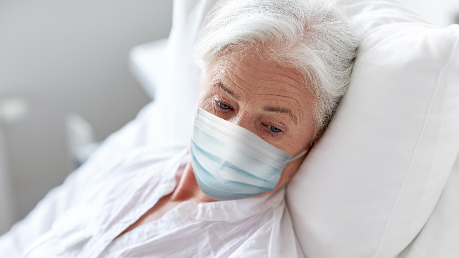 Eine Seniorin liegt mit Maske in einem Krankenbett.