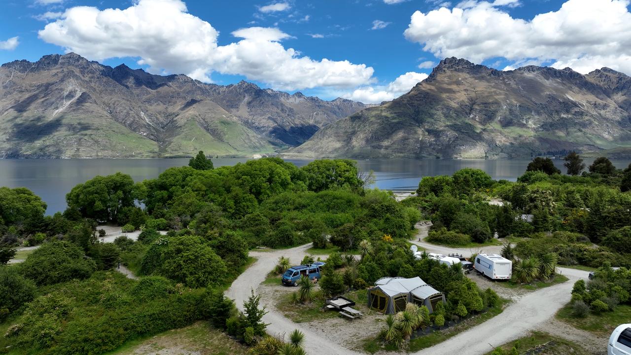 Vor dem Hintergrund von See und Bergen liegt eine Grünfläche, auf der vereinzelt Camping-Wagen stehen. Vor dem Hintergrund von See und Bergen liegt eine Grünfläche, auf der vereinzelt Camping-Wagen stehen.
