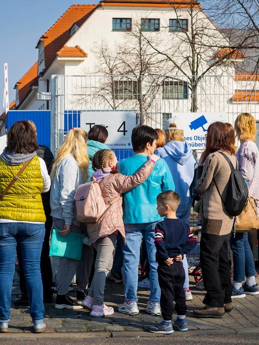 Familien mit Kindern stehen vor einem Zaun.