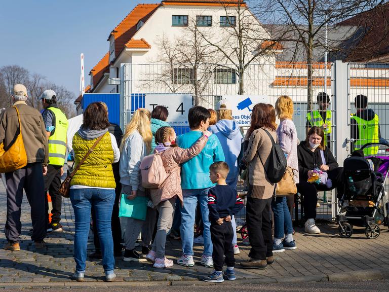 Familien mit Kindern stehen vor einem Zaun.
