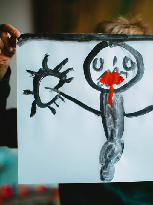 Ein Kind hält ein selbstgemaltes Bild vor seinen Kopf. Dem Mensch auf dem Bild läuft rote Farbe aus dem Mund.