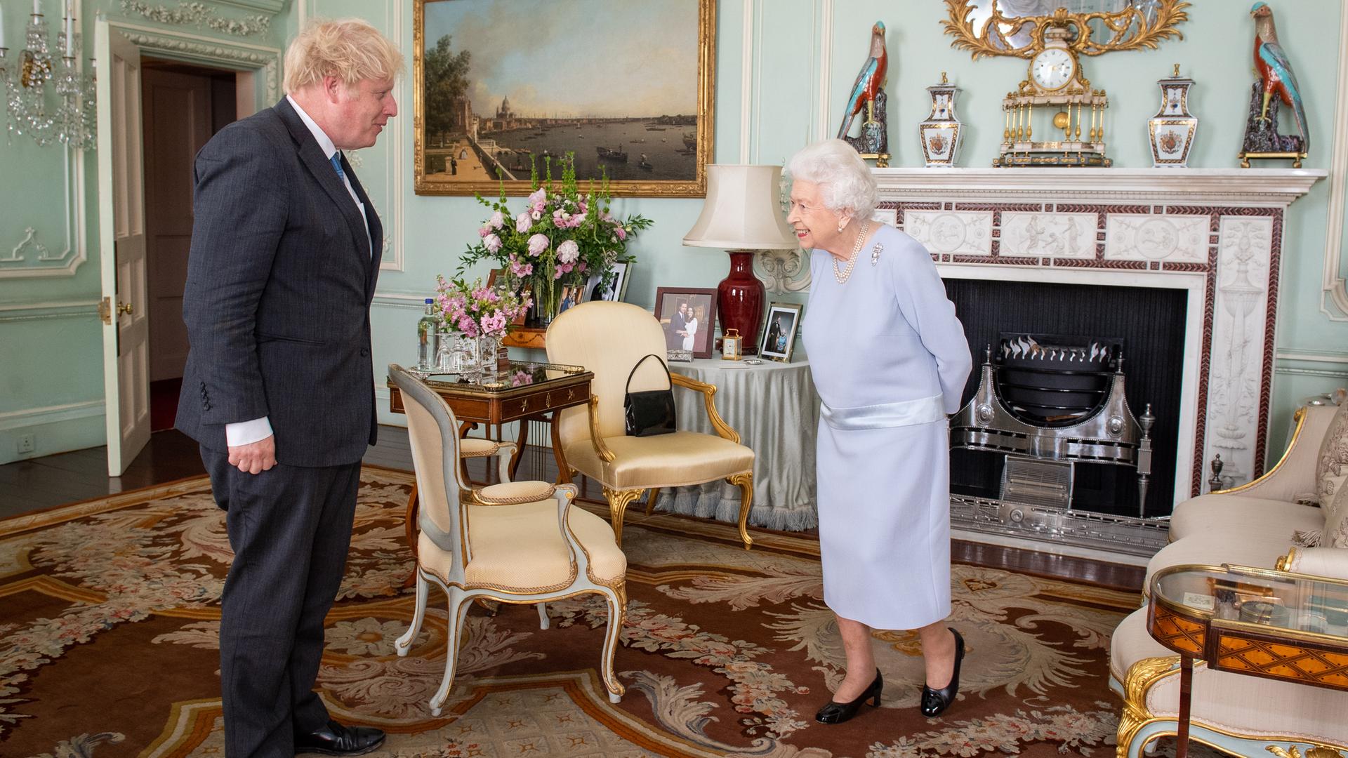 Boris Johnson und die Queen stehen sich gegenüber und sprechen miteinander.