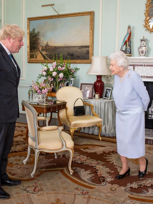 Boris Johnson und die Queen stehen sich gegenüber und sprechen miteinander.