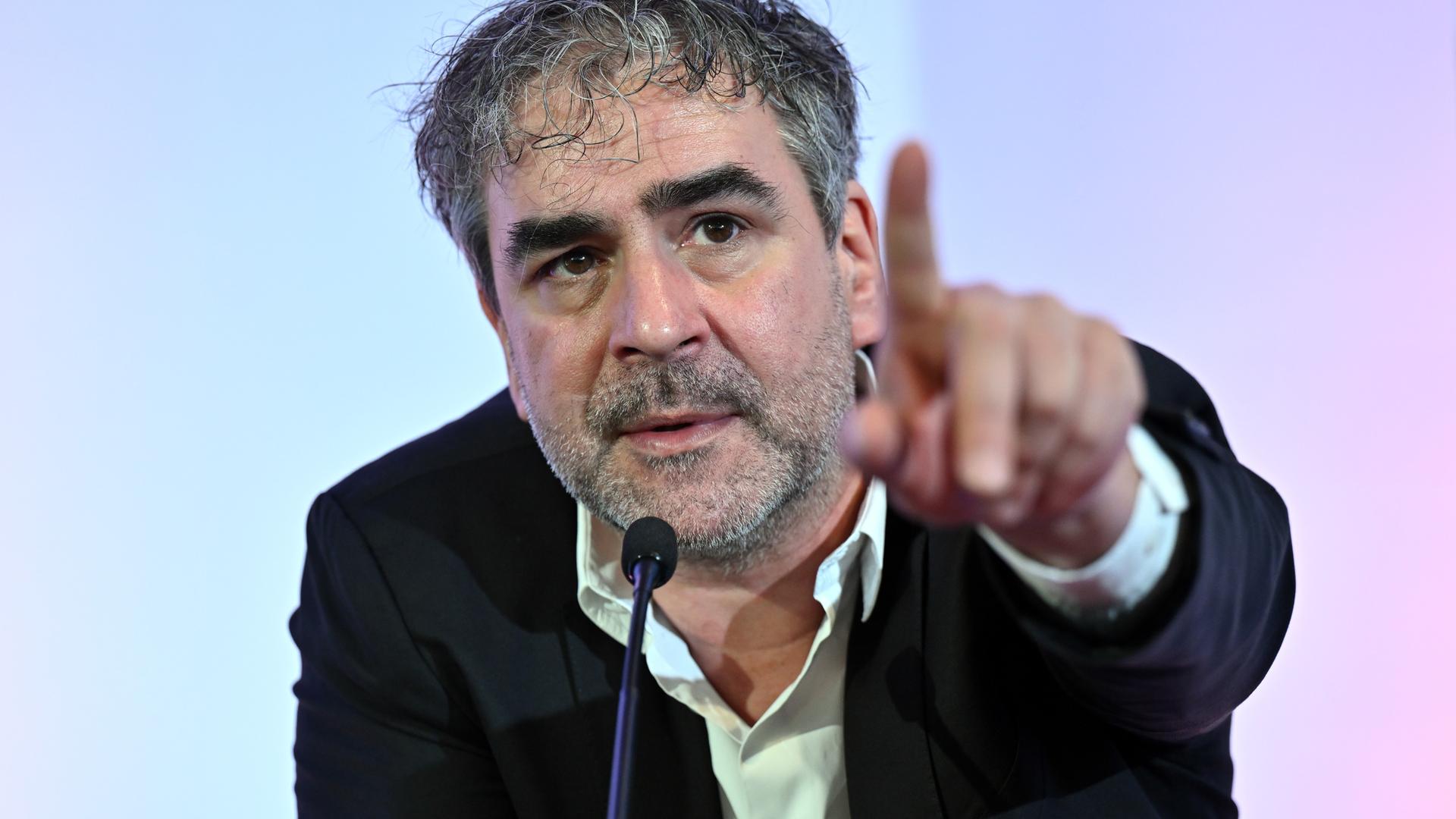 Deniz Yücel spricht in ein Mikrofon und deutet in den Saal. Deniz Yücel spricht in ein Mikrofon und deutet in den Saal.